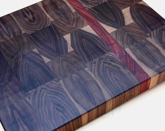 May include: Rectangular end-grain cutting board with a dark blue and brown wood pattern. A thin, red stripe runs down the center. The board is made of various wood pieces, creating a unique design.