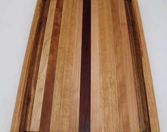 May include: Rectangular wooden cutting board with a variety of wood tones. The board features a juice groove around the perimeter and is constructed from vertical strips of light and dark wood. A dark brown strip runs down the center.