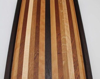 May include: A rectangular wooden cutting board with a dark brown border and a striped interior. The stripes alternate between light and dark shades of brown, creating a visually appealing pattern. The board has a juice groove.