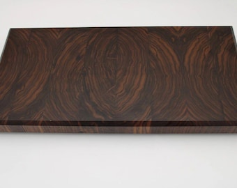 May include: A rectangular wooden cutting board with a dark brown, swirling grain pattern. The board has a smooth, polished surface and a beveled edge. The wood grain creates a visually appealing design, suitable for kitchen use.