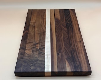 May include: A rectangular wooden cutting board with a dark brown and light wood grain pattern. A vertical strip of light-colored wood runs down the center. The board is made of various wood pieces, creating a unique design.