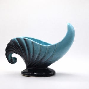 May include: A ceramic cornucopia-shaped vase featuring a glossy finish that transitions from a deep black base and side to a bright turquoise blue interior and upward-curving tip. The exterior surface displays a series of vertical, moulded ridges.