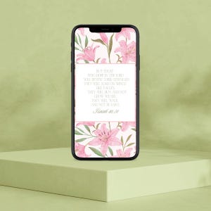 Può includere: Uno smartphone mostra uno sfondo floreale con gigli rosa e foglie verdi. Lo sfondo presenta un rettangolo bianco con testo da Isaia 40:31. Il telefono è su una superficie verde chiaro.