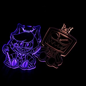 May include: Two acrylic character cutouts with LED lighting. One is purple and features a cat-like character with a staff. The other is orange and has a TV-headed character with a crown. Both have a cartoonish, menacing design.