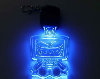 May include: A blue LED keychain featuring a cartoon character with a television screen for a head. The character has an angry expression and is wearing a suit. The keychain has a silver clasp and a black base.