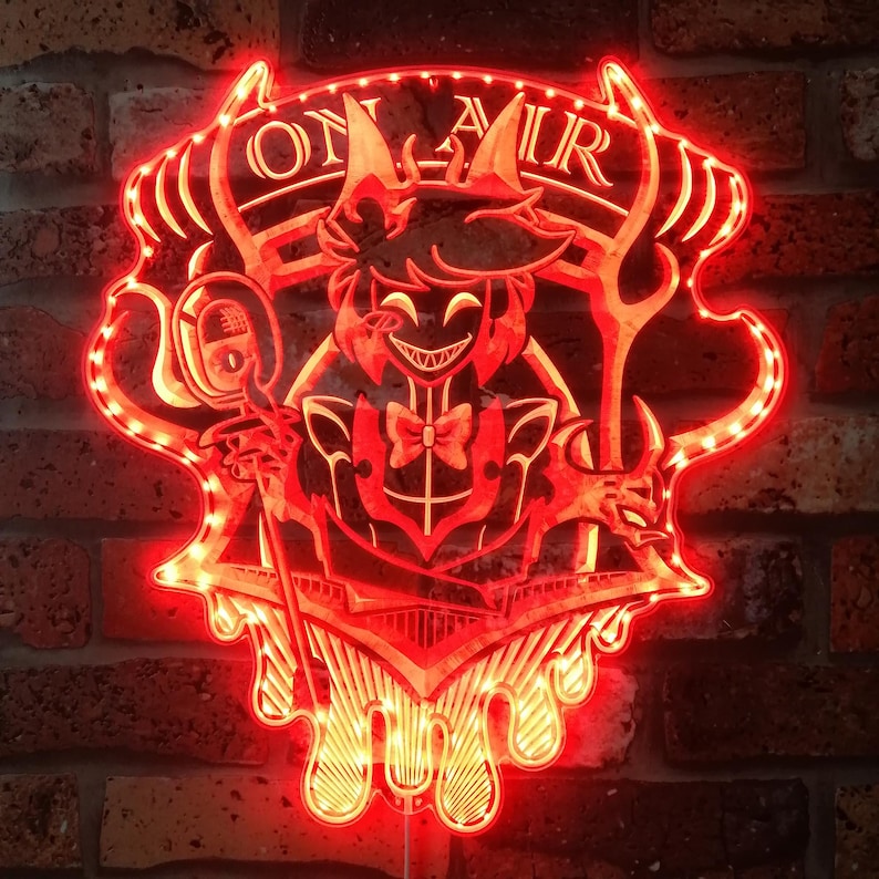 Puede incluir: Un letrero luminoso LED rojo con un personaje de dibujos animados con cuernos, pajarita y micr&oacute;fono. El letrero tiene el texto "ON AIR" y est&aacute; montado en una pared de ladrillo. El letrero est&aacute; iluminado con luces LED rojas.