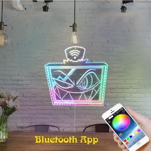 May include: A neon sign with a cartoon face design, outlined with colorful LED lights. The sign is connected to a smartphone displaying a color wheel, controlled by a Bluetooth App. The sign is hanging on a white brick wall.