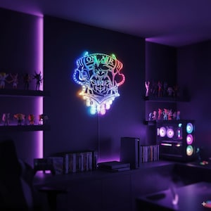 Puede incluir: Una luz de pared LED multicolor en una sala de juegos. La luz tiene la forma de un personaje estilizado con las palabras "ON AIR" en la parte superior. La habitaci&oacute;n es oscura con estantes de figuras y una computadora.