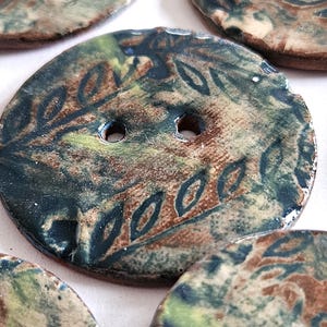 May include: A set of four ceramic buttons with an abstract pattern in brown, green and blue. The buttons have two holes each.
