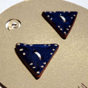 Puede incluir: Dos botones triangulares de cerámica azul con lunares blancos. Los botones tienen un hilo blanco que pasa por los agujeros.