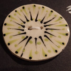 Op de afbeelding: Een witte keramische knoop met een zwart en groen ontwerp. De knoop heeft een zwart-wit stervormig patroon met groene stippen rond de rand.