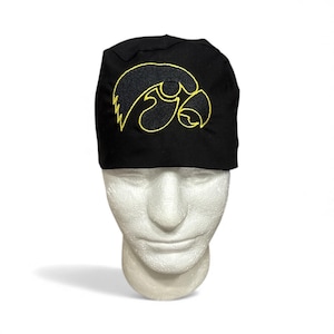 May include: Black beanie with a yellow embroidered hawk logo. The hat is made of a soft material and is displayed on a white mannequin head. The hawk logo is a stylized design with sharp lines and curves.