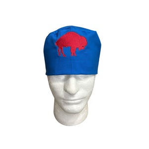 May include: A blue cap with a red embroidered buffalo logo. The cap is made of a soft fabric and is worn on a mannequin head. The cap is a sports-themed accessory.