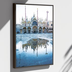 Peut inclure: Impression d'art encadrée de la basilique Saint-Marc à Venise, en Italie, reflétée dans une place inondée. Le bâtiment présente une architecture ornée de dômes et d'arches, peinte dans des tons sourds. L'œuvre est exposée sur un mur blanc.