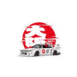 May include: White sticker featuring a stylized race car with the text "LIBERTY WALK" and the number 23. The car is set against a red and white Japanese-style sun design. The sticker has a glossy finish.