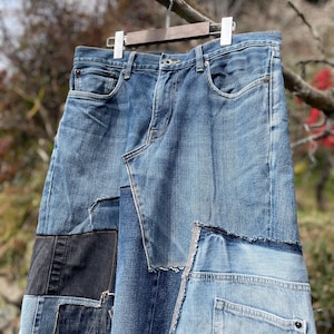 May include: A patchwork denim skirt in various shades of blue, hanging on a wooden hanger. The skirt features a unique design with multiple denim pieces sewn together, including pockets and seams.