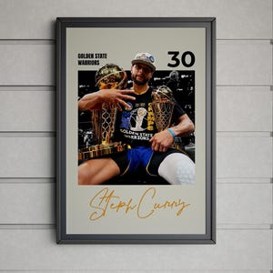 Puede incluir: Póster enmarcado con Steph Curry sosteniendo dos trofeos de campeonato. El póster incluye el texto "Golden State Warriors" y el número "30". El nombre "Steph Curry" está escrito en letras doradas.
