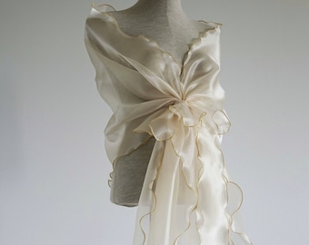 May include: A white sheer shawl with gold trim and scalloped edges. The shawl is draped over a dress form.