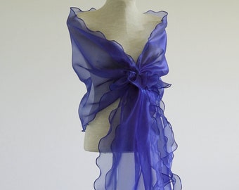 May include: A vibrant purple shawl with a ruffled edge is draped over a mannequin. The sheer fabric is gathered at the back, creating a bow-like detail. The shawl's flowing design adds a touch of elegance.