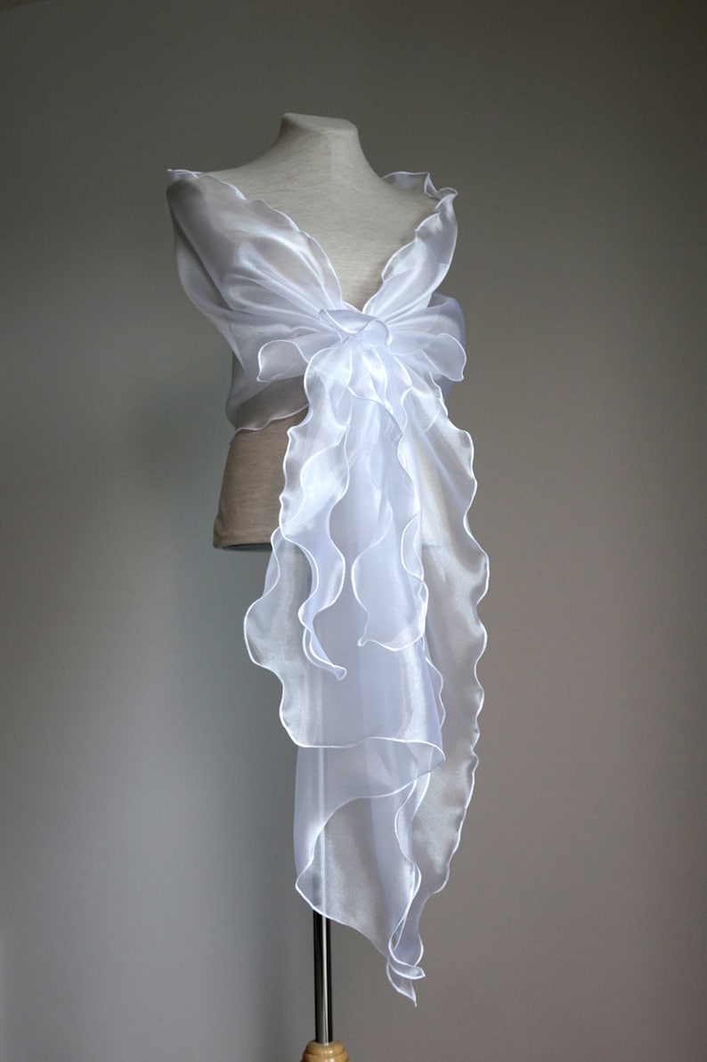 May include: White sheer ruffled shawl with a flowing design. The shawl is draped over a mannequin and is made of a lightweight fabric.