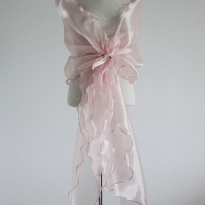May include: A pale pink sheer shawl with ruffled edges, draped over a mannequin. The shawl is tied in a bow at the front.