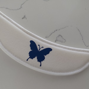 May include: White fabric collar with a blue butterfly design. The collar is curved and has a white trim.