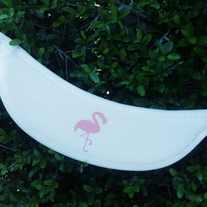 May include: White fabric headband with a pink flamingo silhouette design. The headband is curved and has a soft, flexible texture.