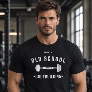 Può includere: Una t-shirt nera a maniche corte con testo bianco che recita Property of Old School Bodybuilding, con una grafica di un bilanciere al centro contenente la parola Crufer. La maglietta ha uno scollo rotondo e un design a vestibilità standard.