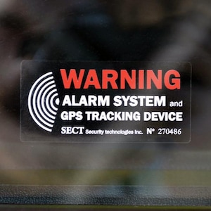 May include: A rectangular sticker with the word "WARNING" in red at the top. Below, it reads "ALARM SYSTEM and GPS TRACKING DEVICE." The sticker also includes the text "SECT Security technologies Inc. N° 270486."