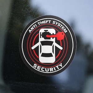 Könnte beinhalten: Runder schwarz-weißer Aufkleber mit den Worten „ANTI THEFT SYSTEM SECURITY“, die eine Autografik und einen roten Schlüssel umgeben. Der Aufkleber ist auf einer Autoscheibe angebracht.
