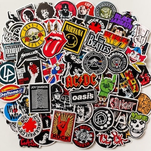 Puede incluir: Una gran colección de pegatinas de vinilo variadas que presentan diversos logotipos de bandas de rock y metal, portadas de álbumes e iconos musicales. Las pegatinas muestran diversas formas, colores y tipografías, incluyendo nombres como Nirvana, AC/DC y The Beatles.