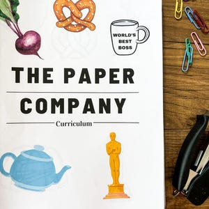 Może przedstawiać: Biała kartka papieru z czarnym napisem "THE PAPER COMPANY" i "Curriculum". Papier zawiera ilustracje buraka, precla, kubka z napisem "WORLD'S BEST BOSS", czajnika i statuetki Oscara. Kolorowe spinacze do papieru i zszywacz są rozrzucone.