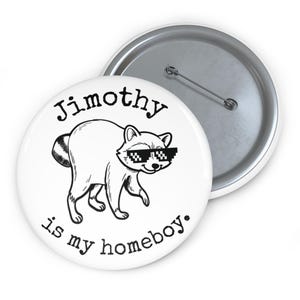 Op de afbeelding: Een ronde witte button met een zwarte lijntekening van een wasbeer die een gepixelde zonnebril draagt. De tekst boven de wasbeer luidt Jimothy en de tekst eronder luidt is my homeboy. De achterkant toont een metalen speldmechanisme.