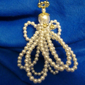 May include: A white beaded angel ornament with gold accents. The angel is made of white pearls and has a gold halo and wings.