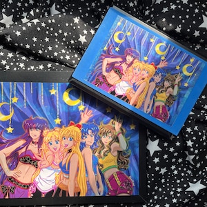 Può includere: Cinque personaggi anime con lunghi capelli biondi e abiti colorati si trovano davanti a uno sfondo blu e viola con lune crescenti dorate e stelle. I personaggi sorridono e salutano.