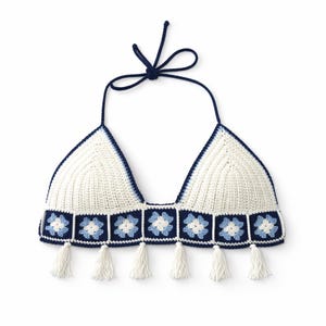 Puede incluir: Top halter de ganchillo blanco con ribete y lazo azul marino. El top presenta una fila de cuadrados florales azules y blancos a lo largo del borde inferior, con borlas blancas colgando. El top tiene forma de triángulo.