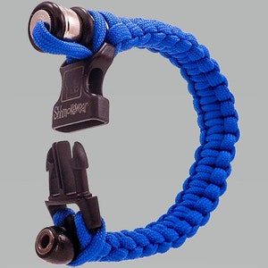 May include: A blue paracord bracelet with a black buckle and a silver whistle attached. The bracelet has the text "Shmoklewear" on the buckle.