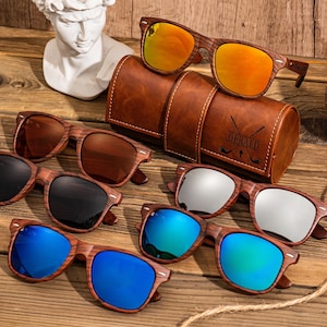 Puede incluir: Seis pares de gafas de sol de madera con lentes de diferentes colores. Las gafas de sol est&aacute;n dispuestas en una fila sobre una superficie de madera. Las gafas de sol est&aacute;n todas en un marco de madera marr&oacute;n. Las lentes son azules, verdes, plateadas, negras, marrones y naranjas.