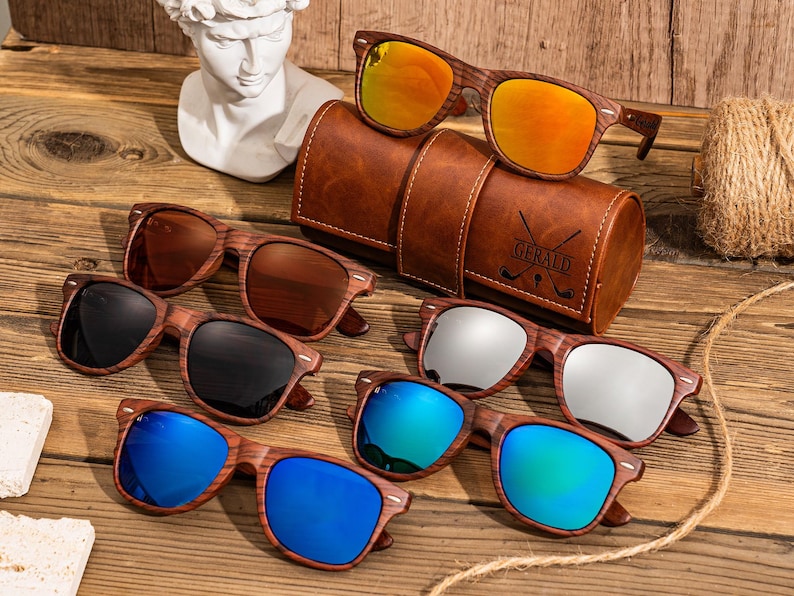 Puede incluir: Seis pares de gafas de sol de madera con lentes de diferentes colores. Las gafas de sol est&aacute;n dispuestas en una fila sobre una superficie de madera. Las gafas de sol est&aacute;n todas en un marco de madera marr&oacute;n. Las lentes son azules, verdes, plateadas, negras, marrones y naranjas.