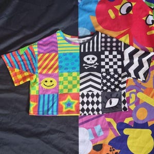 Puede incluir: Una camiseta de manga corta estilo patchwork. Una mitad presenta patrones geométricos coloridos, una carita sonriente y una estrella. La otra mitad tiene diseños en blanco y negro, incluyendo una calavera y un tablero de ajedrez.