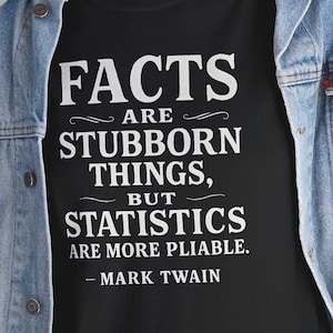 Puede incluir: Camiseta negra con la cita "FACTS ARE STUBBORN THINGS, BUT STATISTICS ARE MORE PLIABLE. - MARK TWAIN" en letras blancas. La camiseta se lleva con una chaqueta vaquera azul.