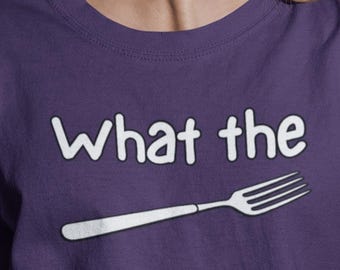 Peut inclure: Un t-shirt violet avec l'inscription "What the" et un dessin de fourchette en blanc. La personne porte un jean rayé bleu et blanc et une veste rouge.