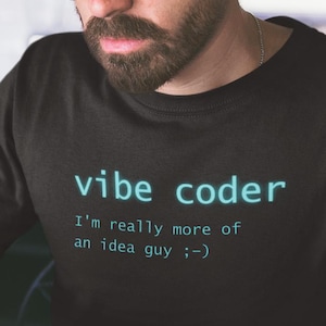 Könnte beinhalten: Schwarzes T-Shirt mit dem Text "vibe coder" in türkisfarbener Schrift. Das Shirt hat auch den Text "I'm really more of an idea guy ;-) ". Die Person auf dem Bild trägt eine Brille und arbeitet an einem Laptop.