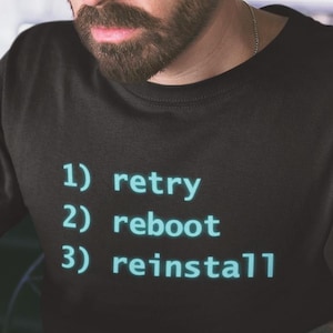 May include: A black t-shirt with the text "1) retry 2) reboot 3) reinstall" in a teal font. A man with glasses and a beard is sitting at a table with a laptop and a glass of liquid.