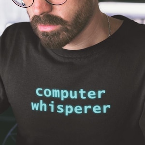 Może przedstawiać: Czarny t-shirt z napisem "computer whisperer" w turkusowej czcionce. Osoba nosi okulary i używa laptopa. Szklanka mrożonej kawy stoi na stole.