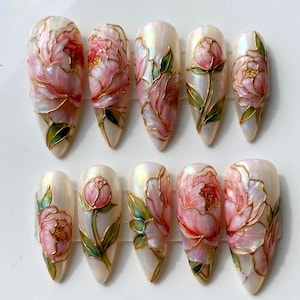 May include: A set of ten almond-shaped artificial nails. Each nail features a pearlescent base with a hand-painted design of pink peonies with gold outlines and green leaves. The nails are arranged in two rows of five.