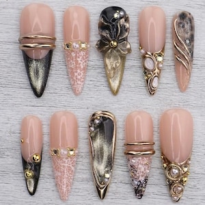 Uñas postizas largas almendradas con forma de ojo de gato en oro negro, flor 3D, perlas y cromo. Un lujoso y glamuroso diseño de uñas hecho a mano para fiestas y bodas.