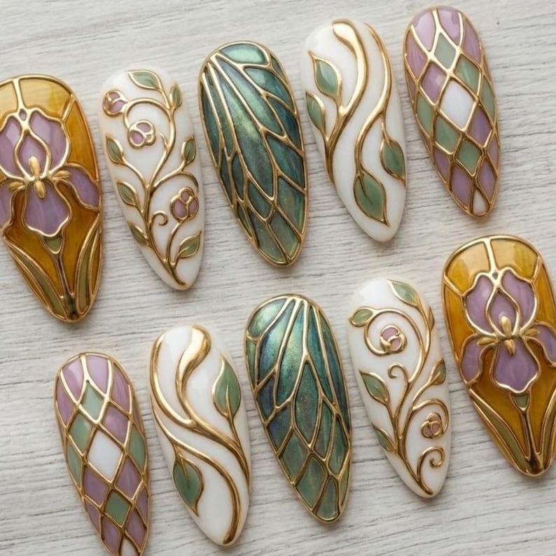 May include: A collection of ten almond-shaped, painted fingernails. Each nail features intricate designs in gold, white, green, purple, and yellow. The designs include floral patterns, geometric shapes, and stylized leaf motifs, all with a glossy finish.