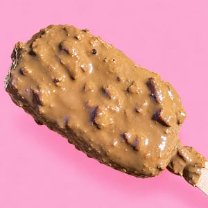 Può includere: Un gelato rettangolare su uno stecco di legno, completamente ricoperto da uno spesso strato di cioccolato al latte liscio color marrone chiaro, con scaglie di cioccolato fondente visibili incastonate sulla superficie, su sfondo rosa.