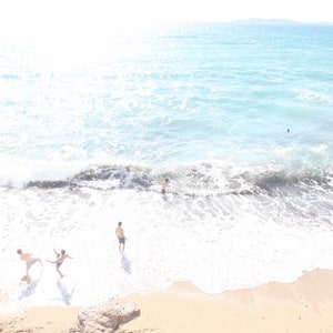 May include: A group of people are enjoying a day at the beach. The water is clear and blue, and the sand is white. The people are all wearing swimsuits and are having fun in the sun.